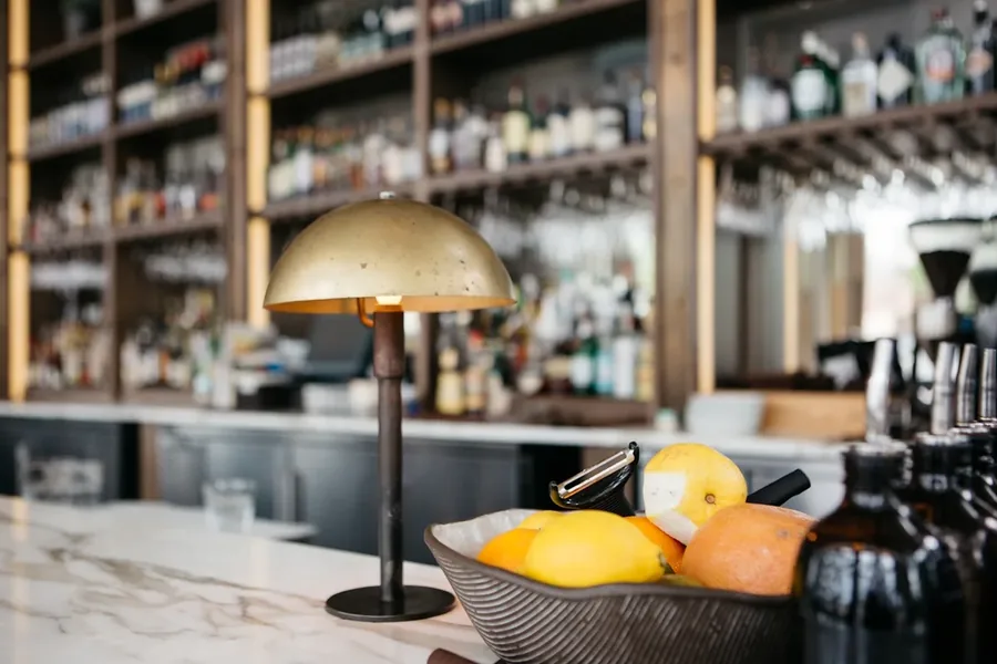 A brass dome lamp on a marble bar top, back bar shelving behind