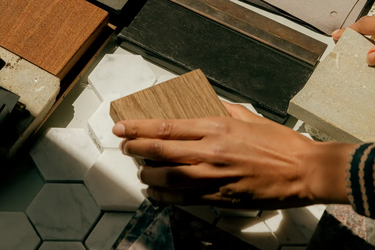 A hand holding a timber sample over hexagonal tile and terrazzo